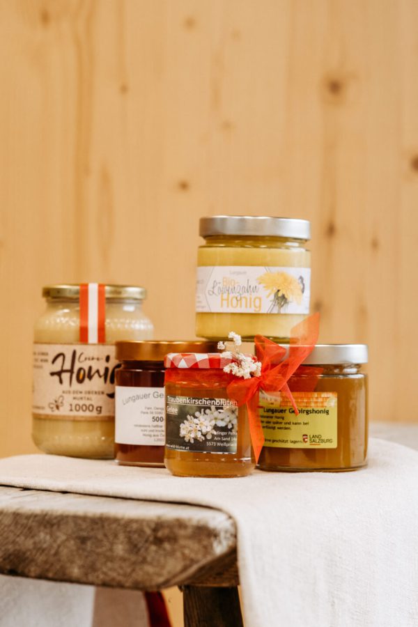 Regionale Honig- und Gelee-Gläser aus dem Lungau auf rustikalem Holztisch vor Holzfond