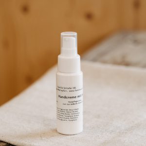 Weiße Flasche Handcreme aus dem Lungau auf Holz- und Stoffuntergrund, regionale Spezialität