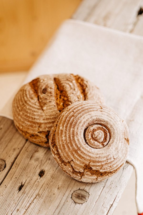 Zwei runde Bauernbrote aus dem Lungau mit rustikaler Kruste auf Holzbrett, regionale Spezialität