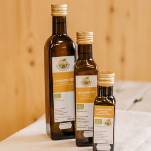 Drei Flaschen Bio-Leindotteröl aus dem Lungau, regional produziert, auf Holztisch platziert