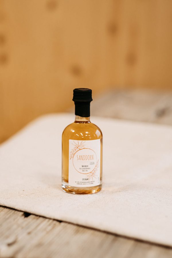 Flasche Sanddornlikör aus dem Lungau auf Holztisch, regionale Spezialität, Hofladen