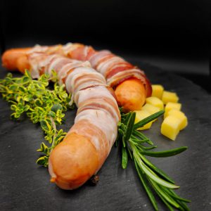 Würstchen mit Speck umwickelt, Kräuter, Käsestücke auf dunklem Schiefer, Lungauer Spezialitäten