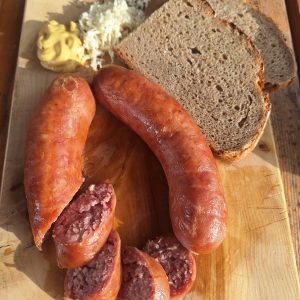 Hausgemachte Wurst mit Bauernbrot, Senf und frisch geriebenem Kren auf Holzbrett