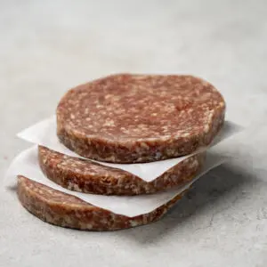 Drei regionale Burgerpatties aus Lungauer Rindfleisch, sauber getrennt, auf hellem Untergrund