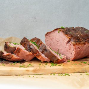Aufgeschnittenes Lungauer Fleischlaibchen auf Holzbrett, bestreut mit frischen Kräutern, regional