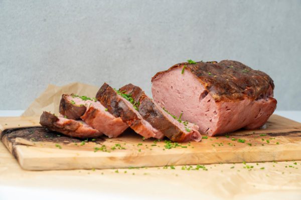 Aufgeschnittenes Lungauer Fleischlaibchen auf Holzbrett, bestreut mit frischen Kräutern, regional