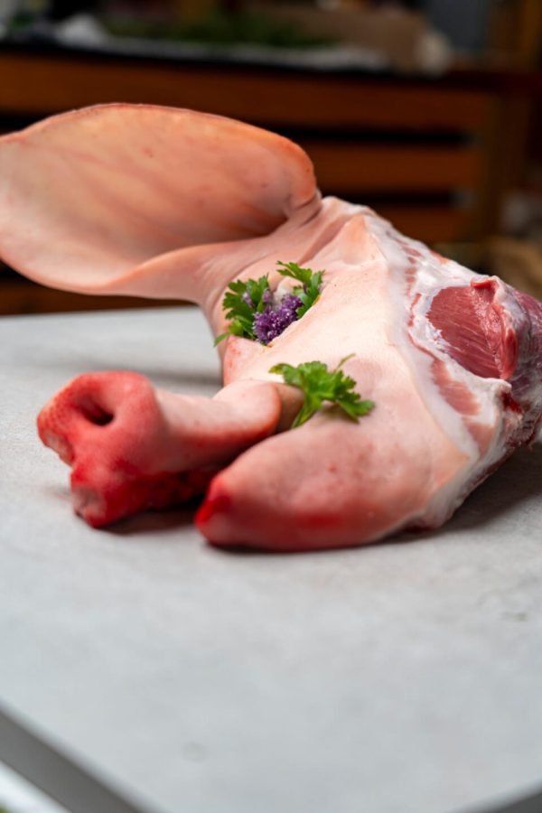 Frisches Schweinekopfstück mit Ohr aus dem Lungau, dekoriert mit Petersilie und Blüte