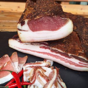 Lungauer Speck auf Schieferplatte mit Pfefferoni und Holzbank im Hintergrund